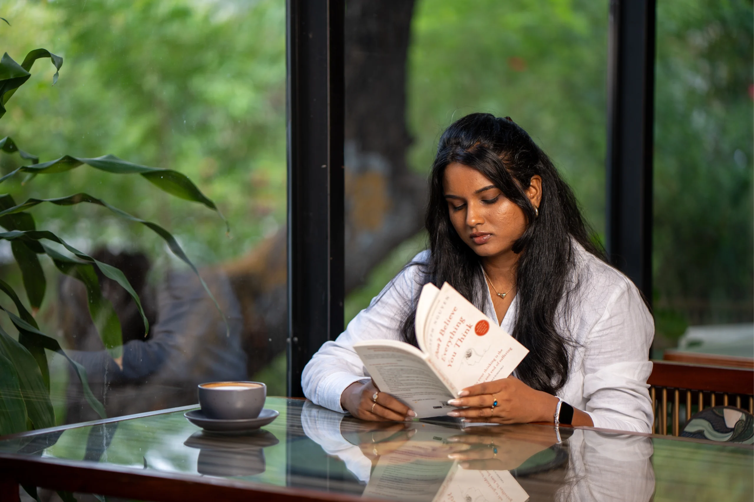 Vijayasanthoshini reading a book at a café table by a window